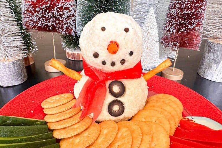 Snowman Cheeseball with pretzel arms, carrot nose, and fruit rollup scarf