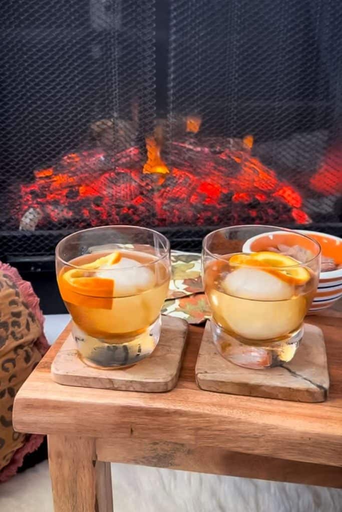two maple bourbon sours in glasses in front of fireplace