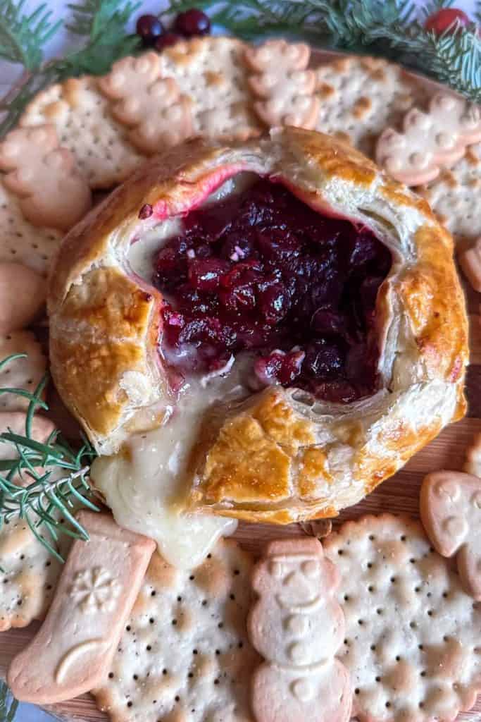 baked brie in puff pastry with star cut out filled with cranberry sauce. Surrounded by crackers